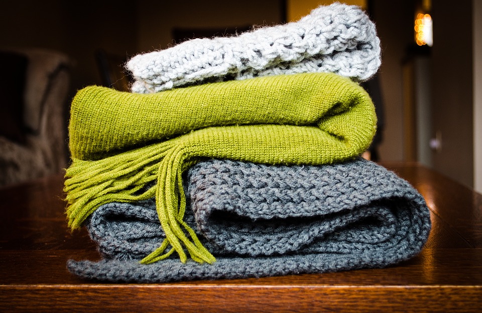 A selection of knitted blankets in light grey, green and dark grey