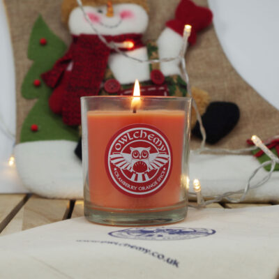 A Cranberry Orange Spice candle in front of a Christmas stocking