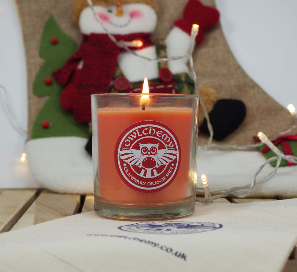 A Cranberry Orange Spice candle in front of a Christmas stocking