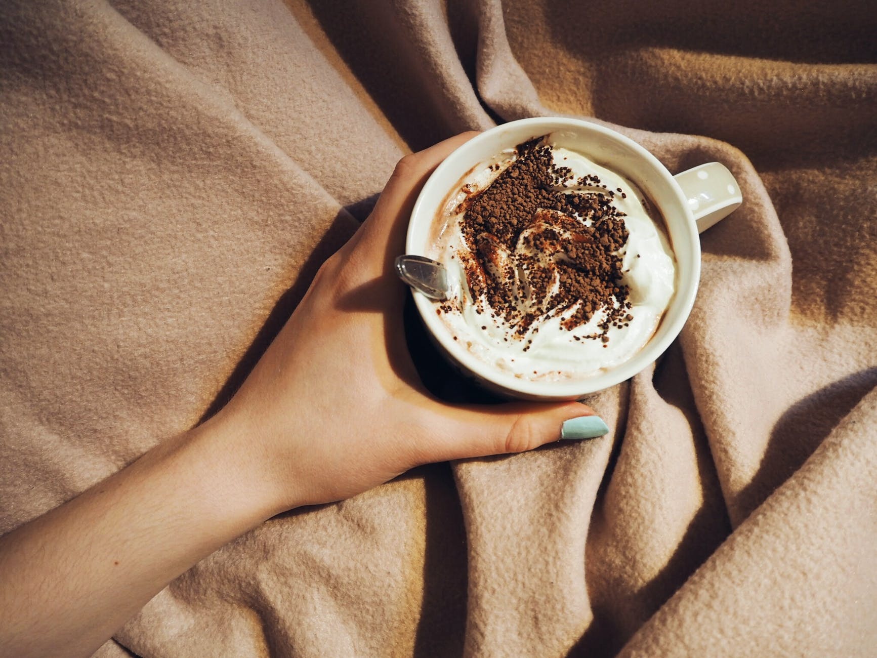 A person tucked up under a blanket holding a hot chocolate