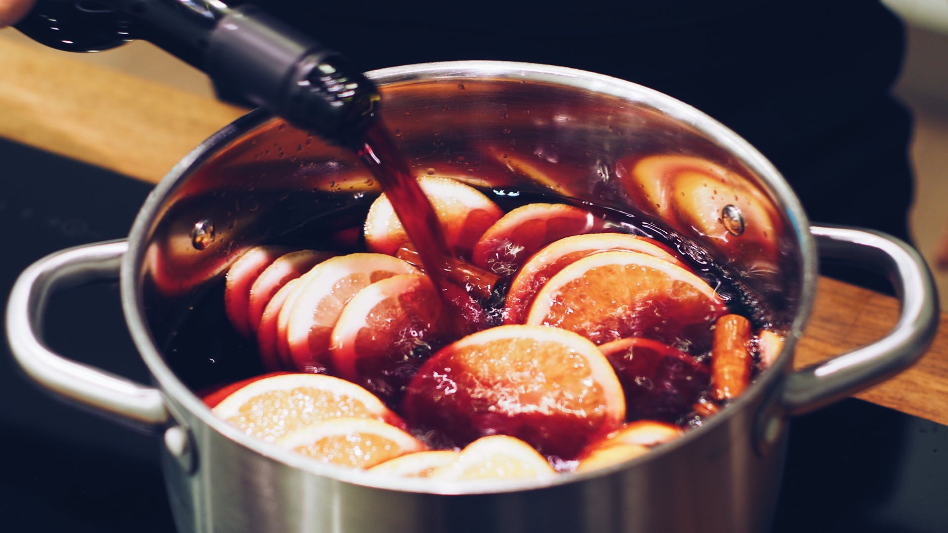 Red wine being poured into a saucepan filled with citrus fruit