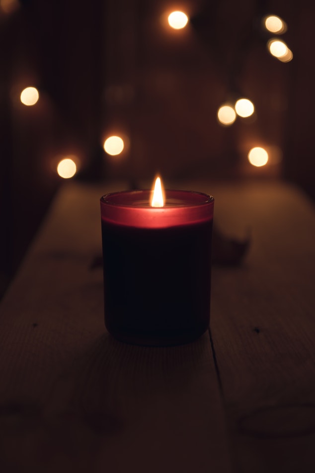 A lit red candle placed on a table in front of some white glowing fairy lights.