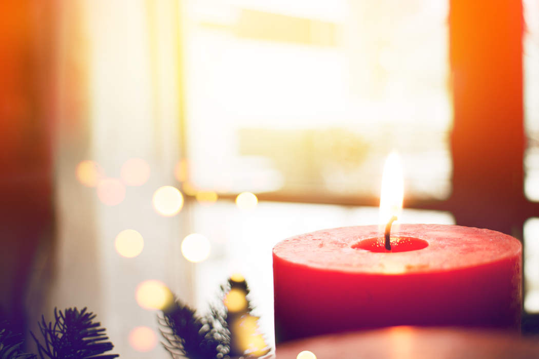 A red candle burning in front of the branches of a Christmas tree.