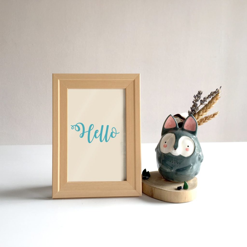 A wooden photo frame next to a china ornament of a bush baby. 