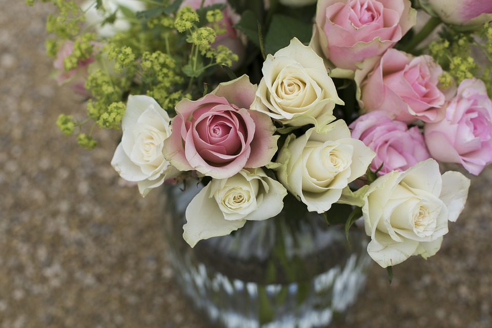 A glass vase filled with cream and pink roses as well as other foliage. 