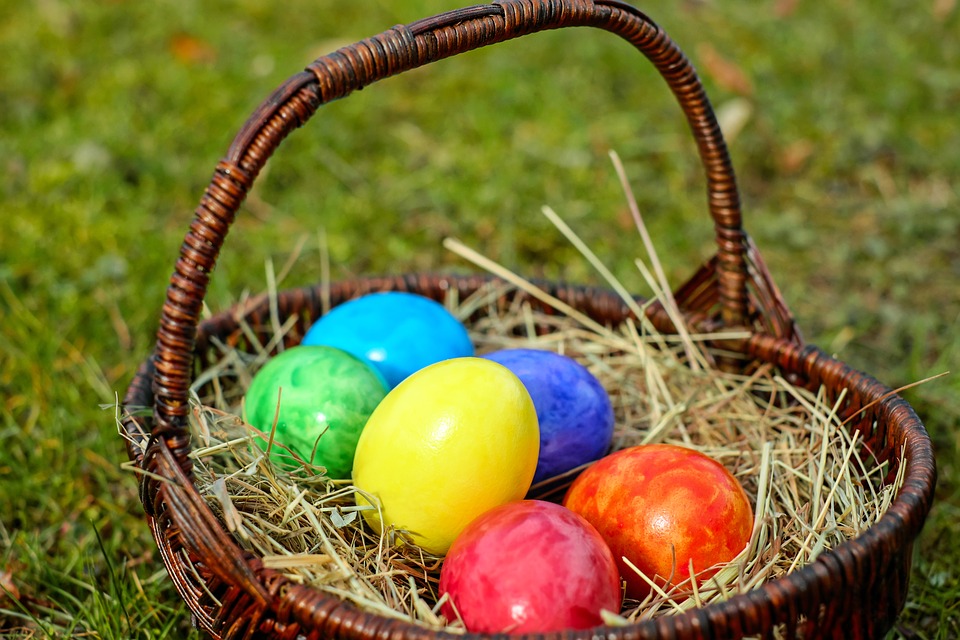 A wooden wicker basket filled with straw and selection of colourful eggs.